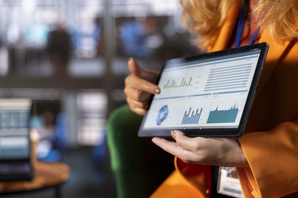 Profissional da área de compras analisando um dashboard de performance em um tablet, com gráficos e métricas de aquisições. A cena representa as etapas de monitoramento e supervisão do ciclo ppms, fundamentais para a gestão estratégica de suprimentos e o controle de resultados.