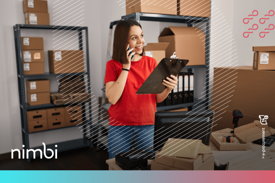 Mulher sorridente usando celular e segurando uma prancheta em ambiente de estoque, com caixas organizadas e computador à frente, representando a organização e acompanhamento da jornada de compras em um processo de e-Procurement.